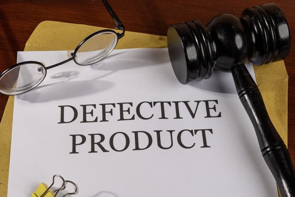 A legal document labeled &ldquo;Defective Product&rdquo; placed on a desk with a judge&rsquo;s gavel, eyeglasses, and file folder, symbolizing product liability law.