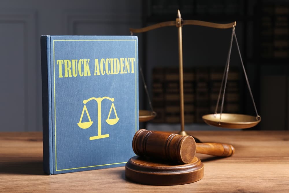 A law book labeled “Truck Accident” sitting on a desk beside a judge’s gavel and brass scales of justice.