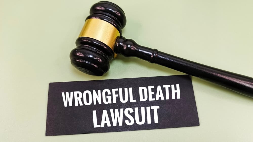 Judge&rsquo;s wooden gavel resting beside a sign that reads &ldquo;Wrongful Death Lawsuit&rdquo; on a green background.