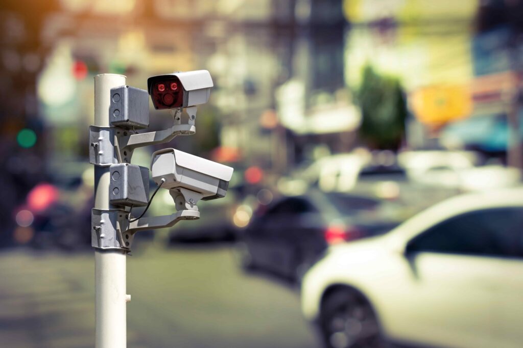 Traffic surveillance cameras mounted on a pole monitoring busy city street traffic for law enforcement and accident investigation Traffic surveillance cameras mounted on a pole monitoring busy city street traffic for law enforcement and accident investigation