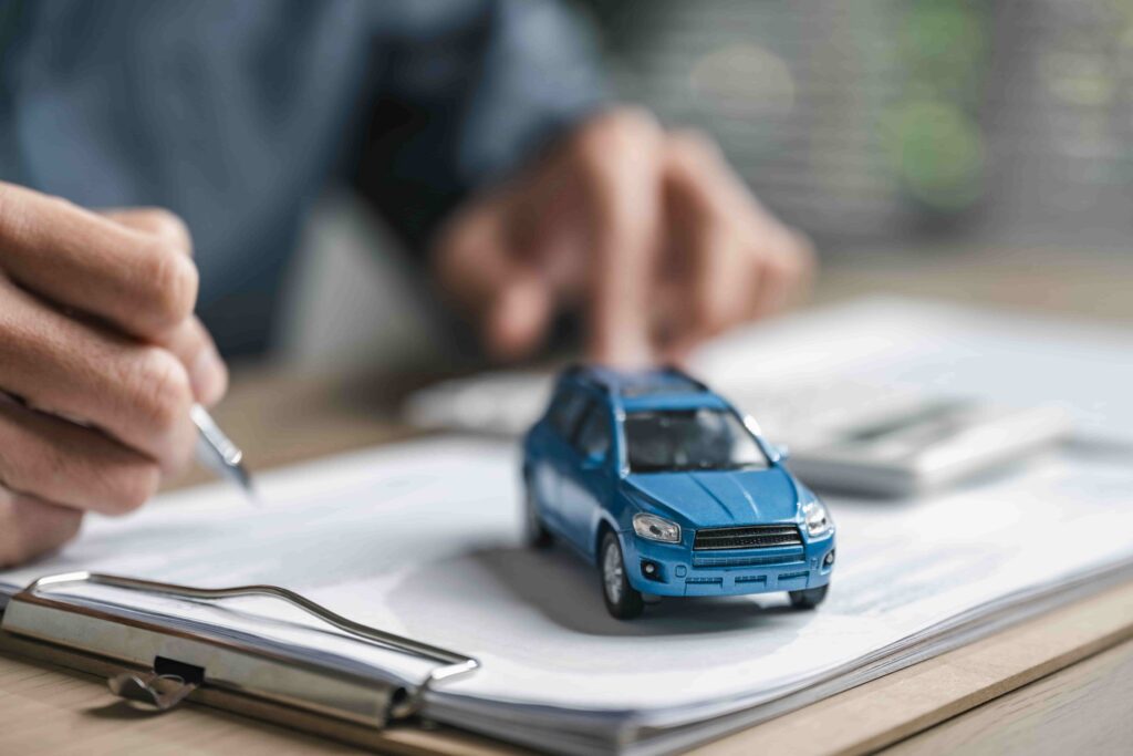 &ldquo;Insurance agent reviewing auto insurance paperwork with a small car model on a clipboard, representing car accident claims and coverage