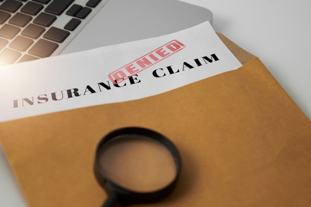 At-fault driver&rsquo;s insurance claim denied letter in envelope with magnifying glass on desk