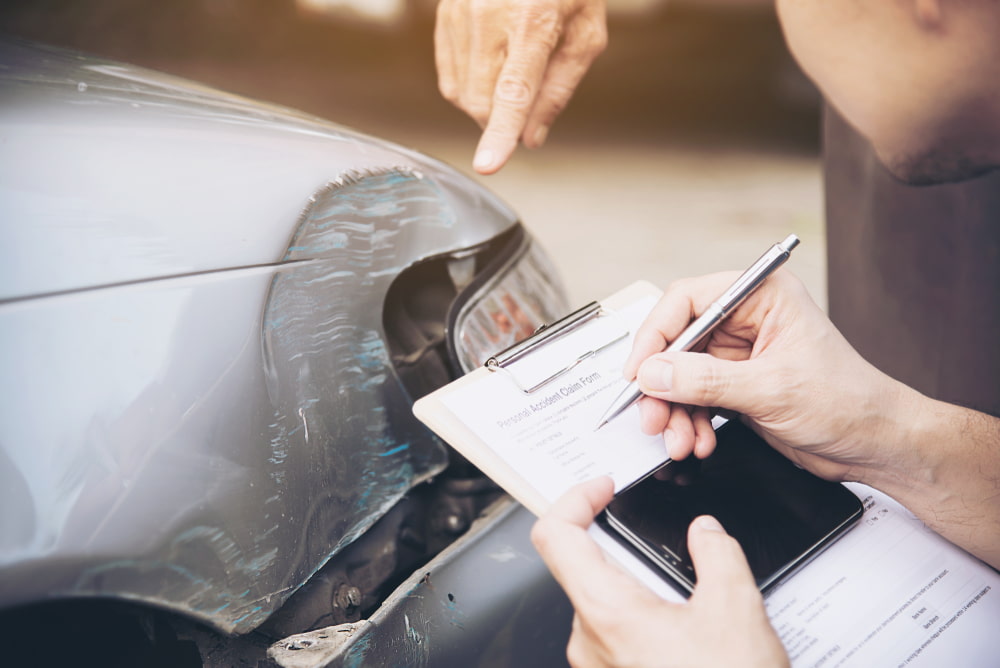Person documenting side damage to a vehicle while reviewing paperwork after a car accident.