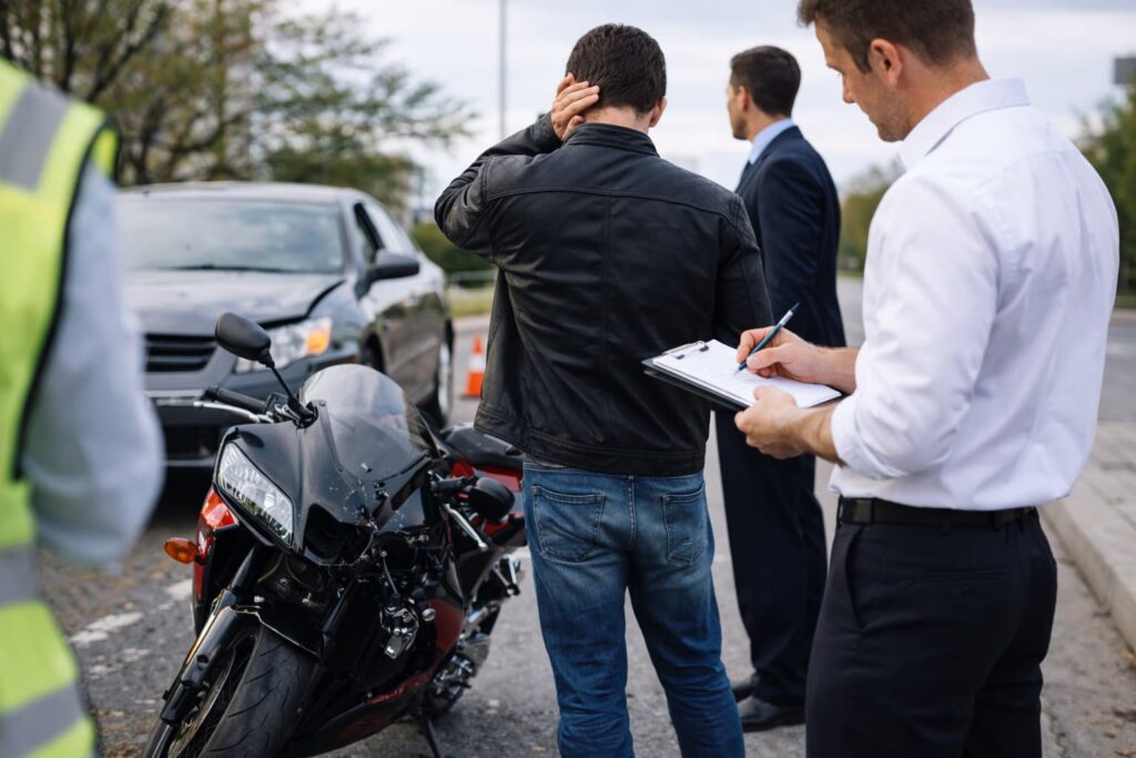 Motorcyclist standing beside a damaged motorcycle after a minor road accident while insurance details are being recorded on a city street