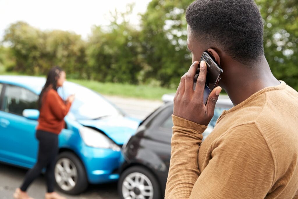 Driver Reporting a Car Accident to Insurance Company Driver calling insurance after a car accident while two damaged vehicles are stopped on the roadside