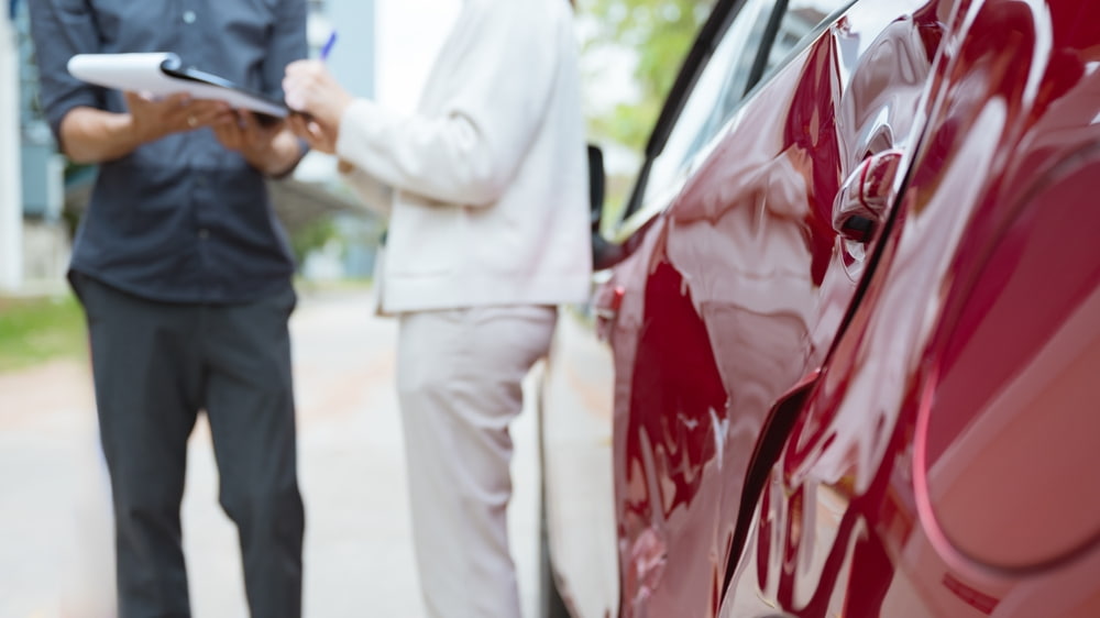 Person documenting side damage to a vehicle while reviewing paperwork after a car accident.