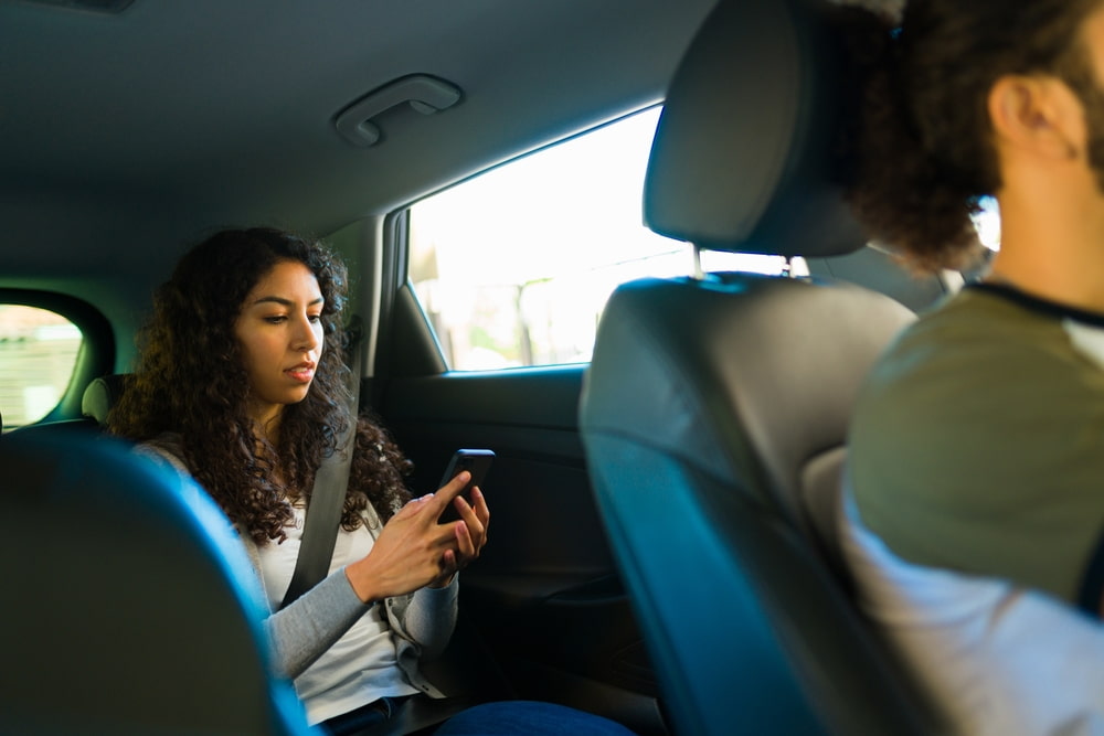 Una pasajera que utiliza un smartphone mientras viaja en el asiento trasero de un vehículo de transporte compartido.