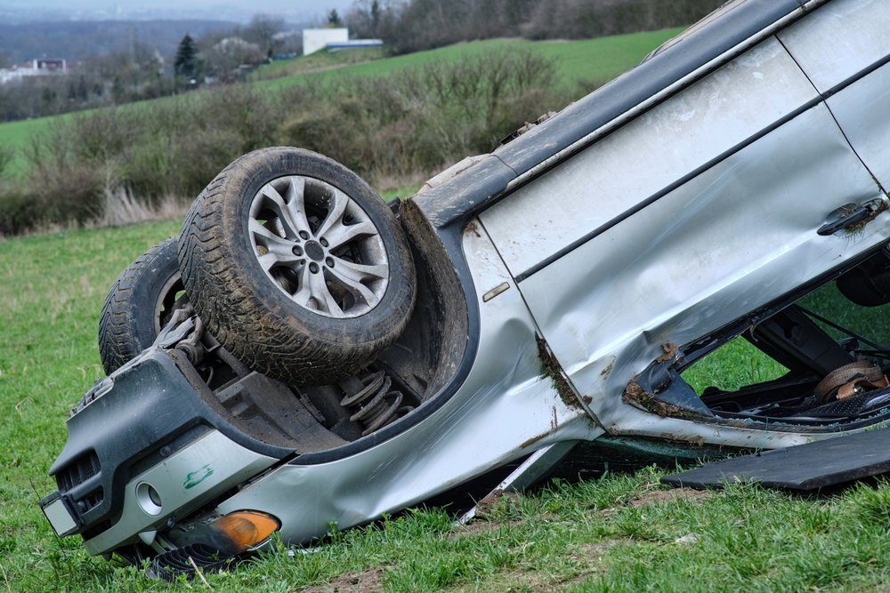 Big SUV car after rollover on the roof in nature. Car crash in agricultural field. Accident on a dusty rural road. Isolated, deformed crashed overturned upside-down vehicle.