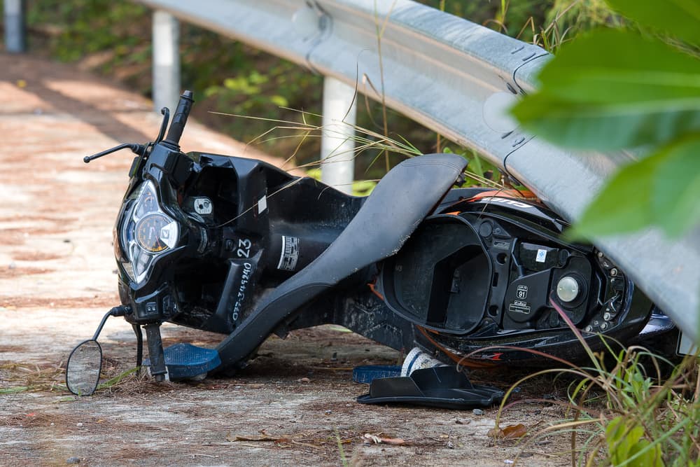Damaged scooter lying beside a roadside guardrail after a crash
