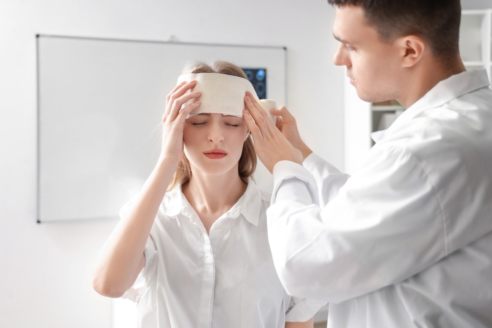 Doctor examining and treating a patient with a bandaged head after a traumatic brain injury.