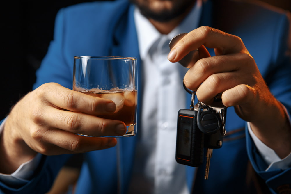 Persona que sostiene un vaso de alcohol y las llaves del coche antes de ponerse al volante