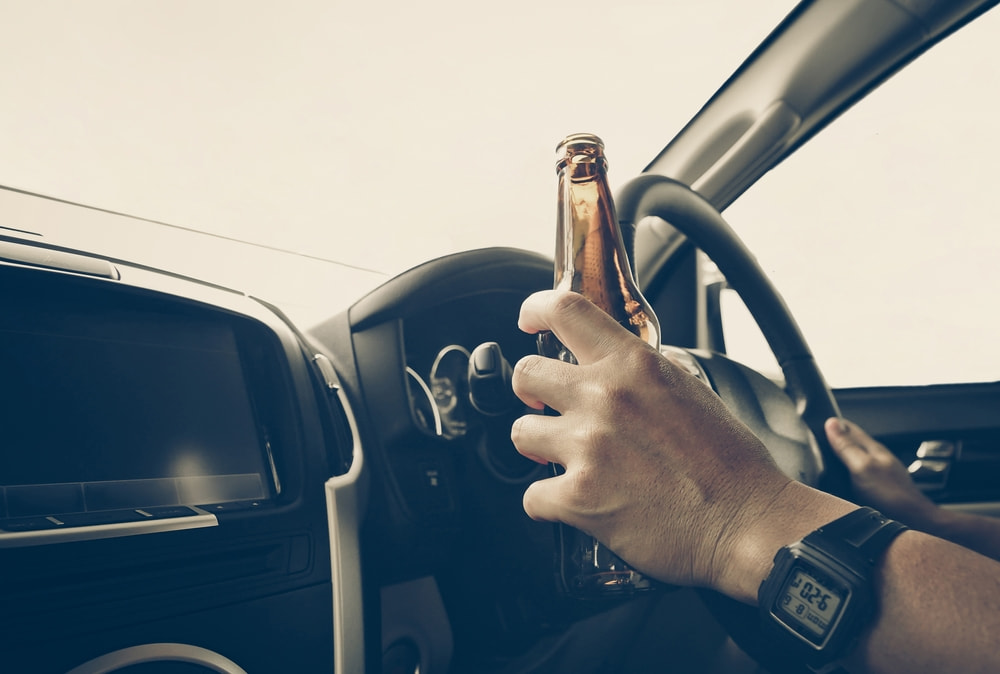 Conductor que sujeta una botella de cerveza mientras conduce un vehículo
