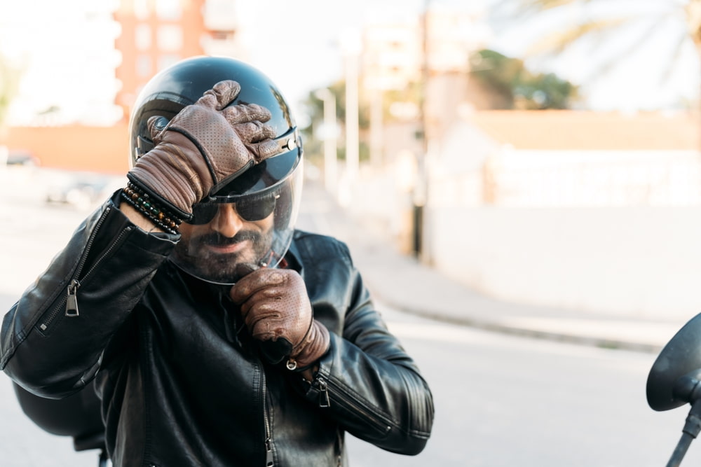 Motorcyclist in a leather jacket closing the visor of his helmet
