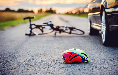 Casco de bicicleta en la carretera, con una bicicleta y un vehículo al fondo tras un accidente