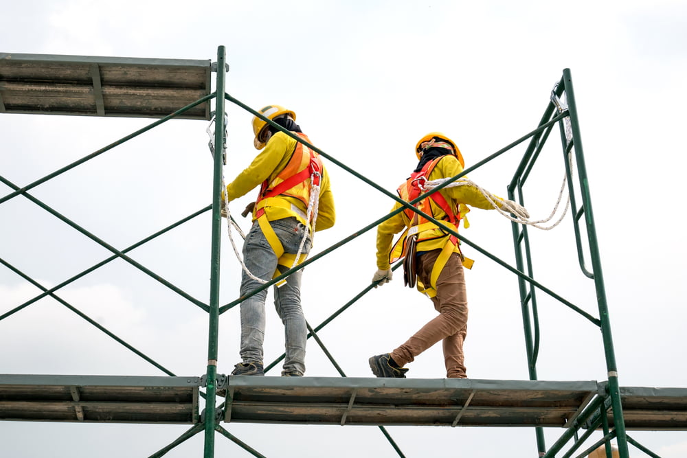 Obreros de la construcción que llevan arneses de seguridad mientras trabajan en andamios elevados en una obra