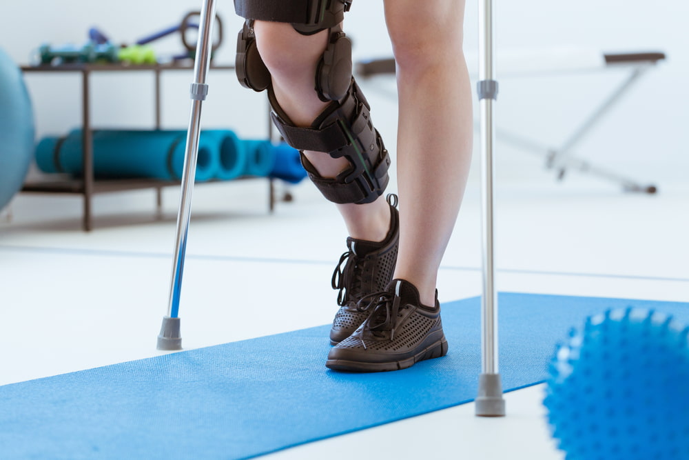 Person wearing a knee brace and using crutches during physical therapy