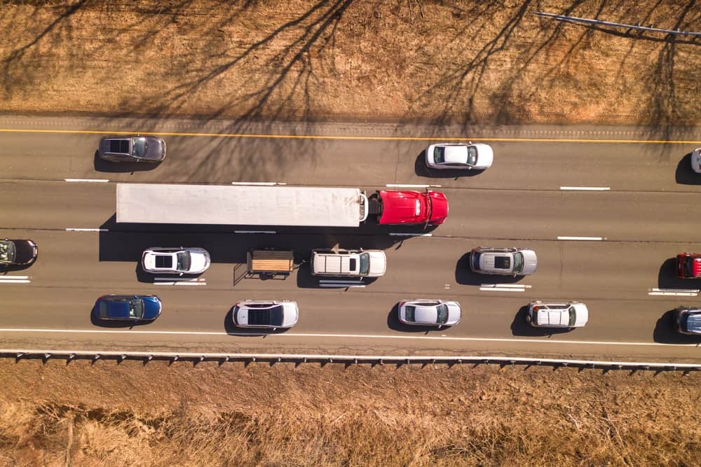 Aerial view of a red semi-truck traveling among passenger vehicles on a multilane highway