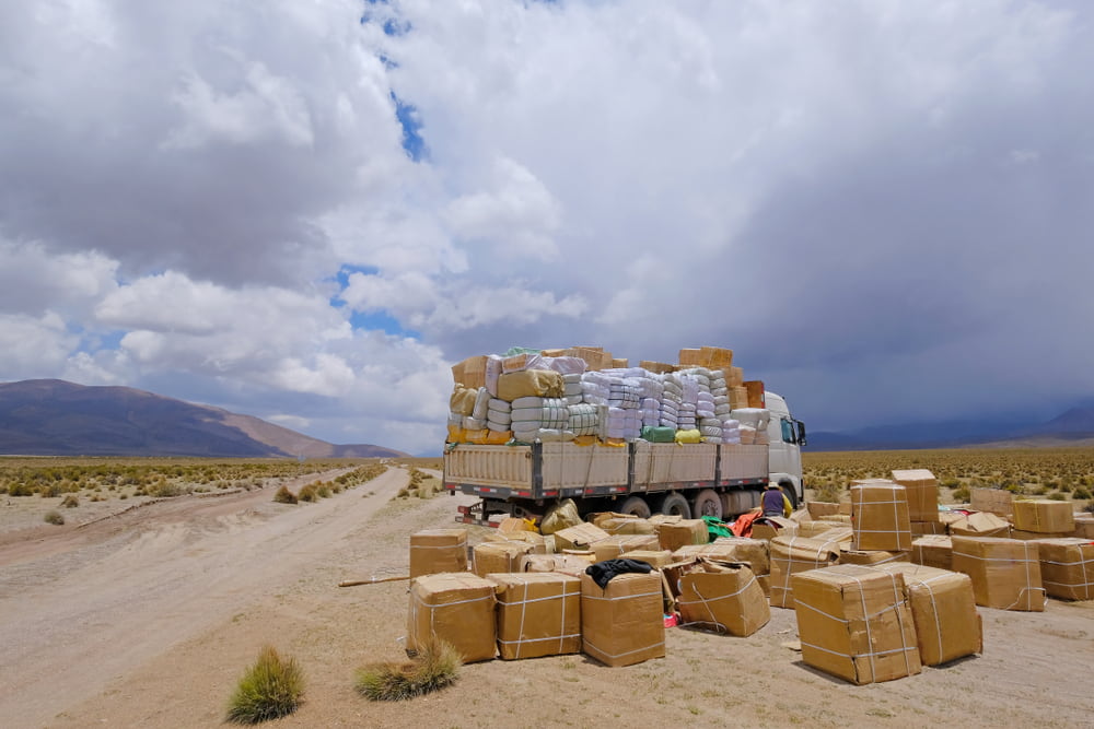 A truck loaded with boxes and wrapped cargo stopped on a desert road under a cloudy sky