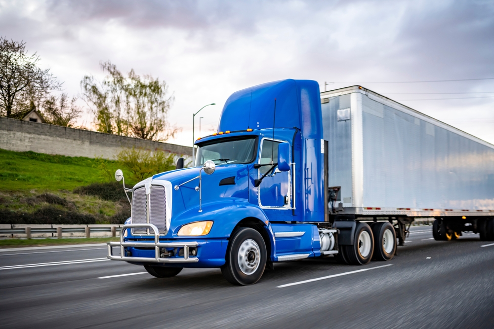 Blue semi-truck driving on a highway with a white trailer