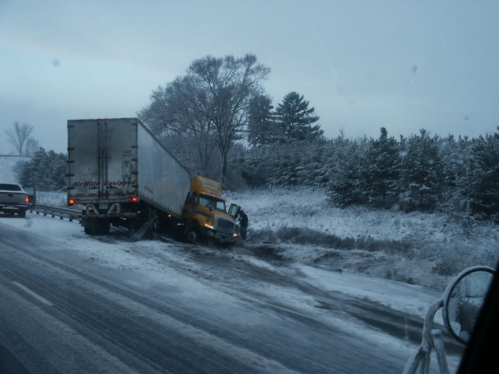 Jackknifed commercial truck off the side of an icy, snow-covered highway.