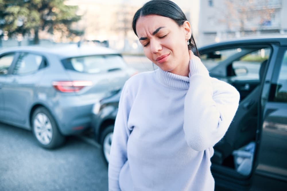 Woman holding her neck in pain while standing beside vehicles after a car accident