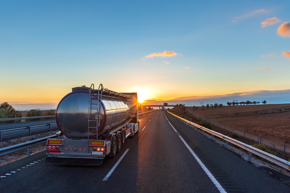 A tanker truck driving down a highway with the sun low on the horizon