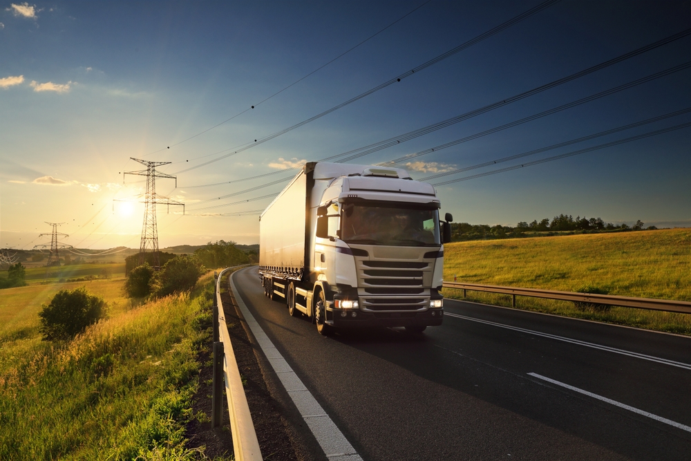 White truck driving on a curving road near power lines at sunset