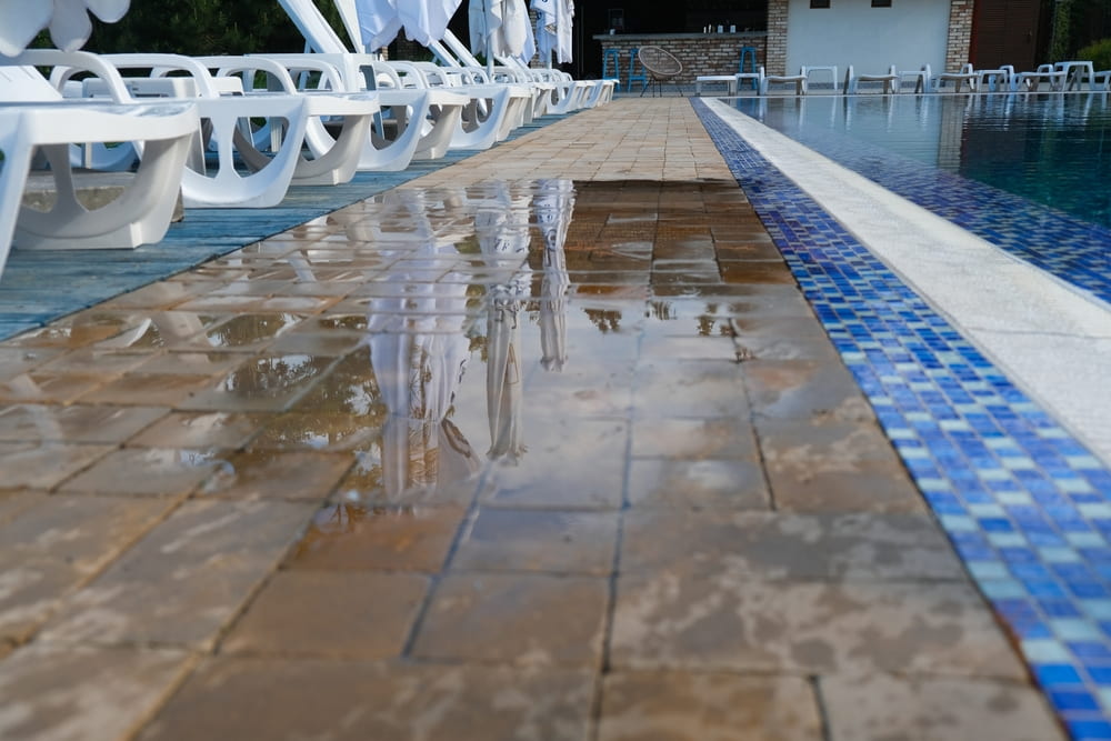 wet tiled walkway beside a swimming pool and rows of lounge chairs